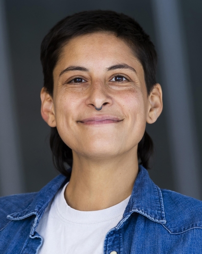 Headshot of light-skinned brown genderqueer person with dark brown mullet and wearing a denim button down shirt over a white tshirt