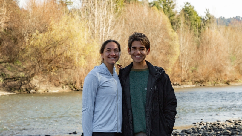 pair of people standing next to each other with river in background